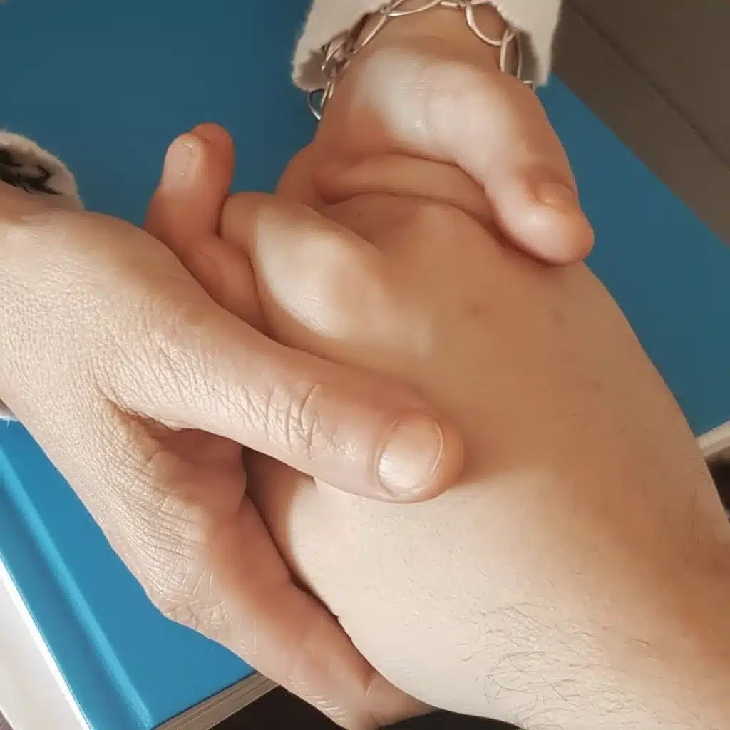 Dos manos entrelazadas sobre libreta azul, simbolizando confianza y apoyo terapéutico.